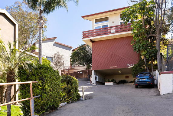 Front view of a multi-story building with a carport and inclined driveway.