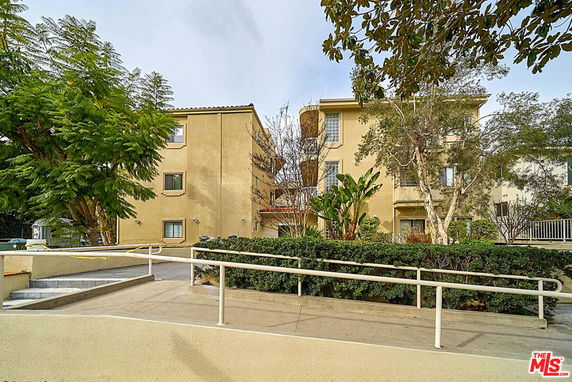 Front view of a multi-story residential building with beige exterior and surrounding vegetation.