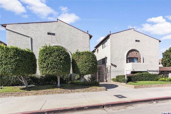 Front view of a multi-story building with arched features and trimmed bushes.
