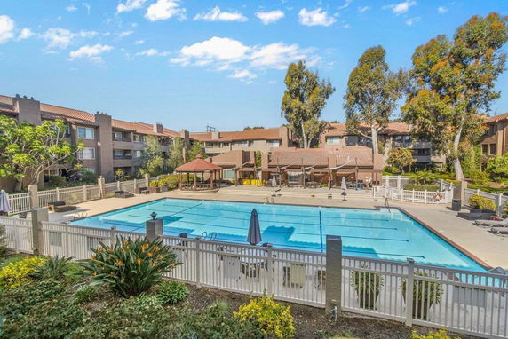 View of an outdoor swimming pool area surrounded by buildings with trees and a gazebo.