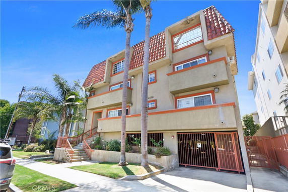 Front view of a multi-story building with a gated entrance and palm trees.