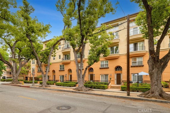 Front view of a multi-story residential building with balconies and tall trees along the street.