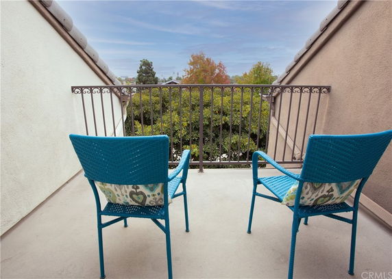 Balcony with two blue chairs overlooking trees and rooftops.