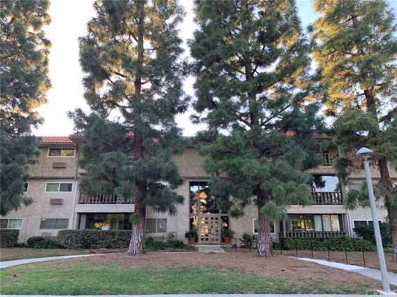 Front view of a multi-story building with balconies and a central entrance, surrounded by tall trees.
