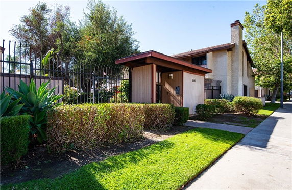 Front view of a two-story house with a gated entrance and surrounding greenery.