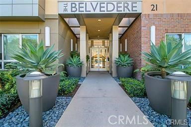 Front view of a building entrance with large potted plants and glass doors.