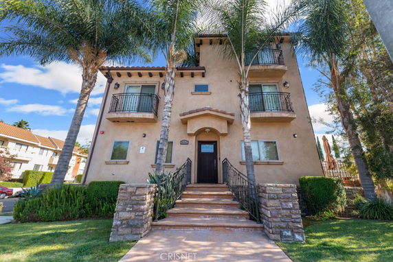 Front view of a three-story house with balconies and palm trees.