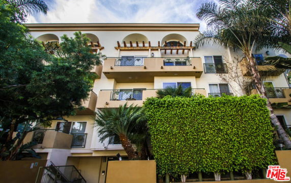 Front view of a multi-story residential building with balconies and greenery.
