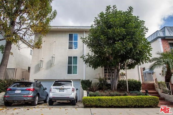 Front view of a multi-story house with parking space and trees.