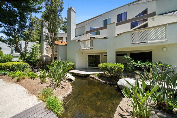 Front view of a multi-story house with balconies and a small pond in the foreground.