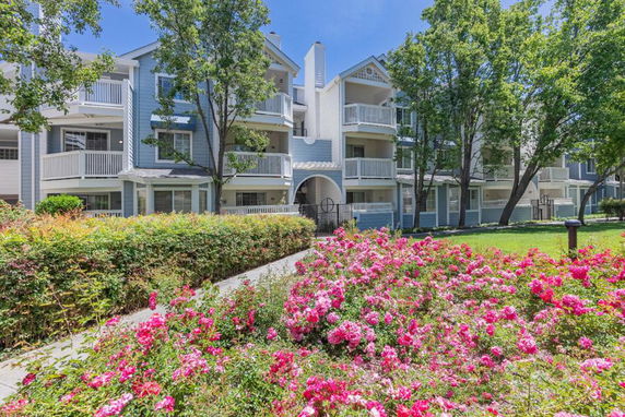 Front view of a multi-story residential building with balconies and a garden in front.