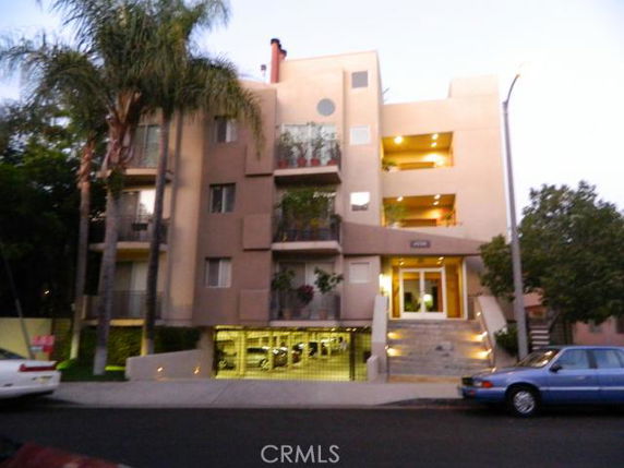 Front view of a multi-story apartment building with balconies and a gated parking area.