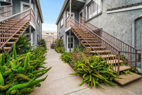 Front view of a two-story building with exterior staircases and greenery.