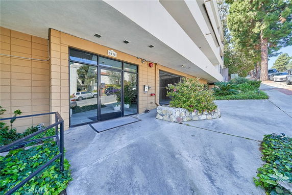 Front view of a building entrance with glass doors and a sloped pathway leading to it.