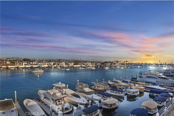 Aerial view of a marina with numerous yachts and boats, and buildings along the waterfront during sunset.