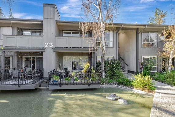 Front view of a two-story apartment building with balconies overlooking a small pond.