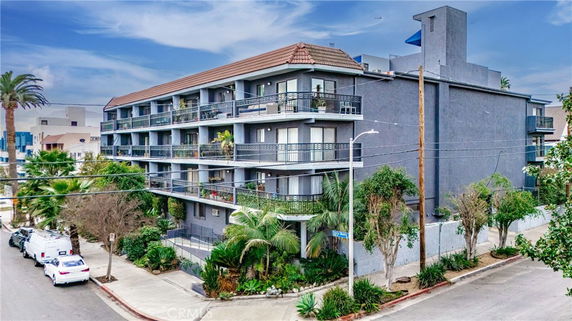 Front view of a four-story apartment building with balconies and a sloped roof.