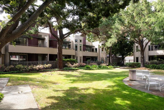 Front view of a multi-story residential building with balconies and surrounding landscaped area.