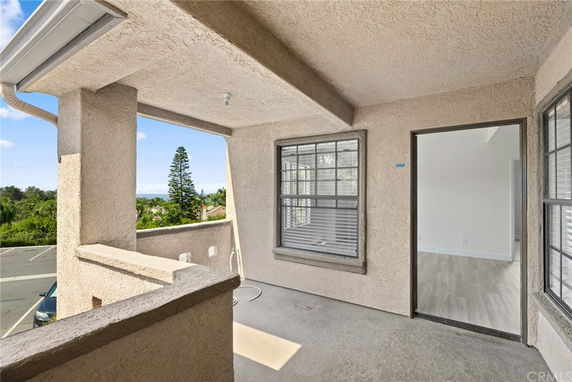 A covered balcony area with views of trees and a distant parking lot.
