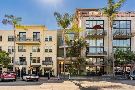 Front view of a multi-story residential and commercial building with balconies and palm trees in front.