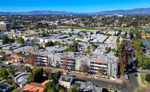 Aerial view of a residential area with multiple apartment buildings surrounded by streets and trees, with mountains in the background.