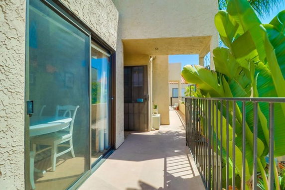 View from a building walkway with sliding glass door and railing overlooking plants.