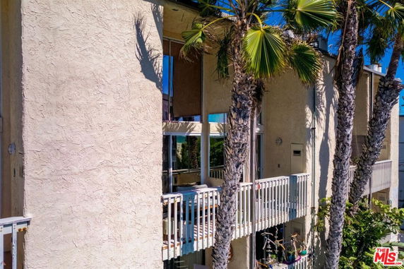 Front view of a multi-story building with a balcony and large windows, partially obscured by palm trees.