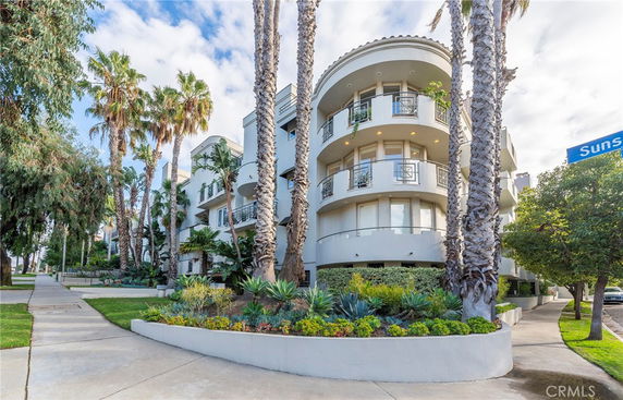 Front view of a multi-story residential building with balconies and surrounded by palm trees.