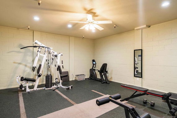 Room equipped with gym and exercise equipment including a multi-station workout machine, exercise bike, and bench.