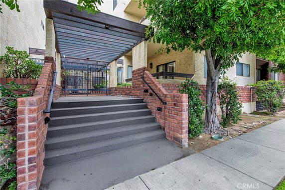 Front view of a building entrance with stairs and a pergola structure.
