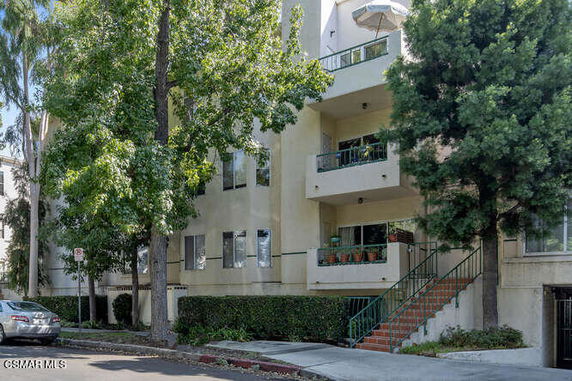 Front view of a multi-story residential building with balconies and stairs leading to the entrance.