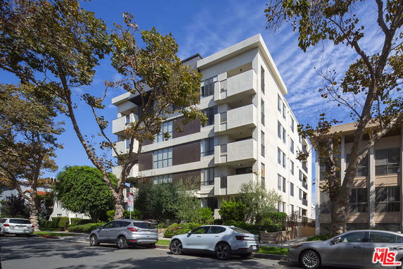 Front view of a multi-story apartment building with balconies and parking area.