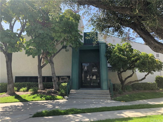Front view of a building with a green entrance and steps, surrounded by trees.
