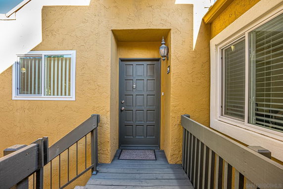 Front entrance of a building with a gray door, yellow walls, and a wooden walkway.