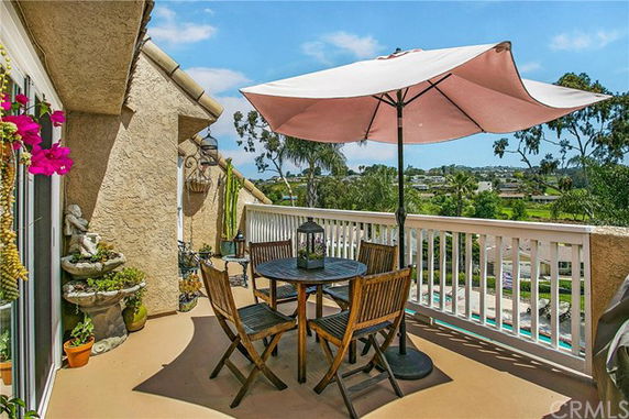 Rooftop patio with an umbrella-covered table and chairs, and views of surrounding greenery.