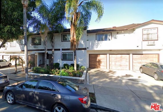 Front view of a two-story residential building with garages and palm trees.