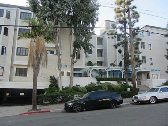 Front view of a multi-story apartment building with trees and cars parked in front.
