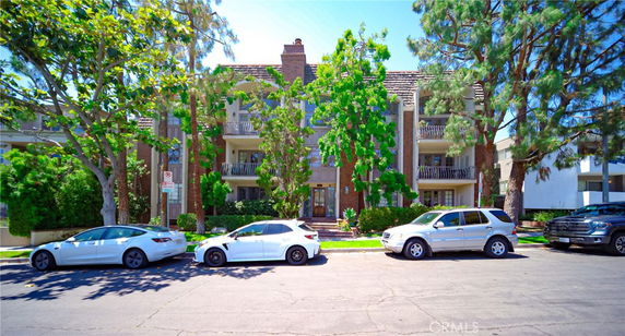Front view of a multi-story residential building with balconies and parked cars in front.