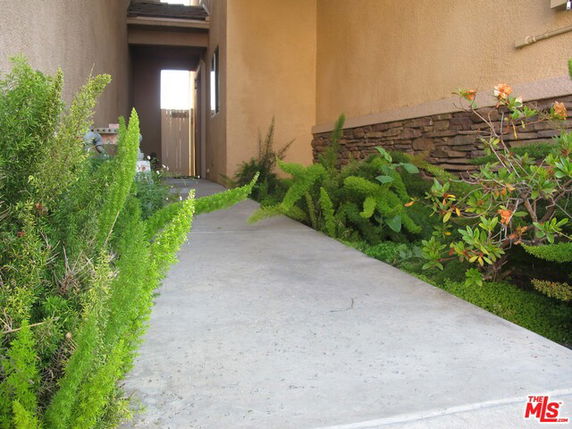 Side view of a house entrance with a pathway and greenery.
