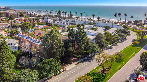 Panoramic view of buildings and coastline with a road lined by trees.