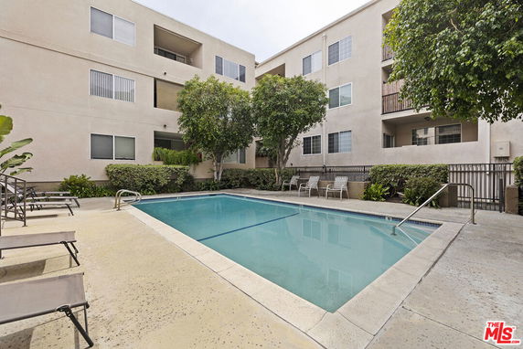 Outdoor swimming pool area surrounded by a multi-story apartment building.