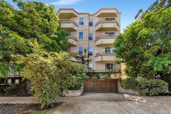 Front view of a multi-story residential building with balconies and surrounding trees.