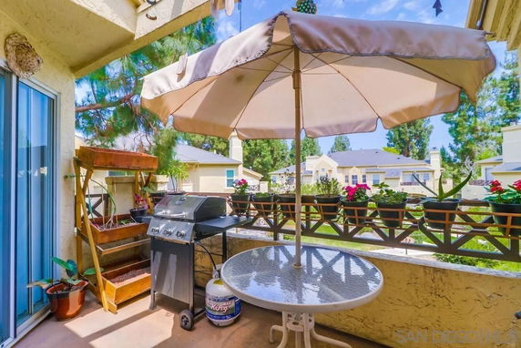 Outdoor balcony with a table, umbrella, and a grill, overlooking nearby residential buildings.
