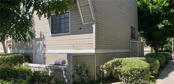 Side view of a multi-story house with beige siding and a small patio area