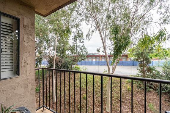 View from a balcony showing a railing, trees, and a fenced area in the background.