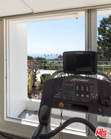 Interior view of a gym with a treadmill facing large windows.