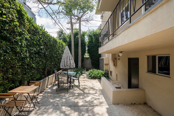 Outdoor patio area with folding chairs, table, and umbrella adjacent to a building with greenery.