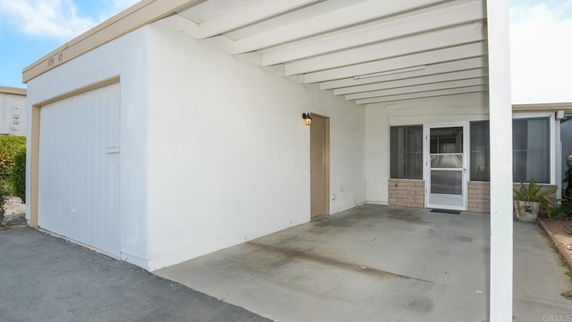 Covered parking area beside a building with a garage door and entrance.