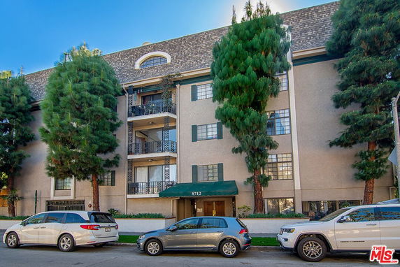 Front view of a multi-story residential building with balconies and trees.