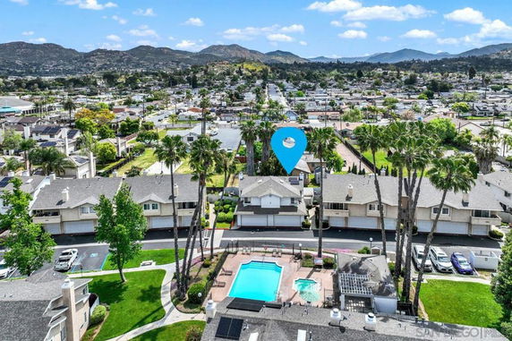 Aerial view of a residential area with townhouses and a communal swimming pool, surrounded by hilly landscape.